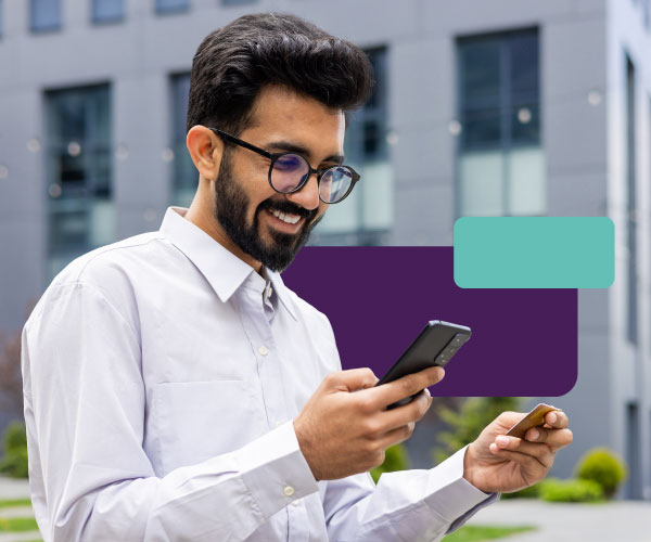 A professional in business casual attire checks their phone with a satisfied expression, with a debit card in their hand.